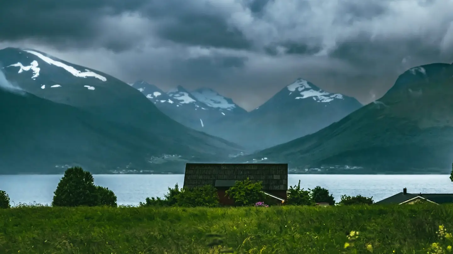A weathered barn stands amid lush summer meadows on the shore of a Norwegian fjord near Mauseidvagen on the island of Sula, More og Romsdal.