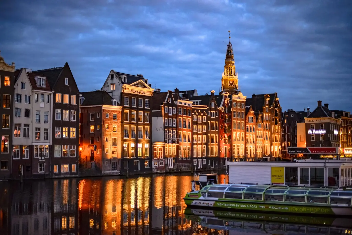 Amsterdam's Damrak canal houses glow amber and gold against a deepening blue twilight sky in this HDR composition, their stepped and neck gables reflected in the dark harbour basin below.