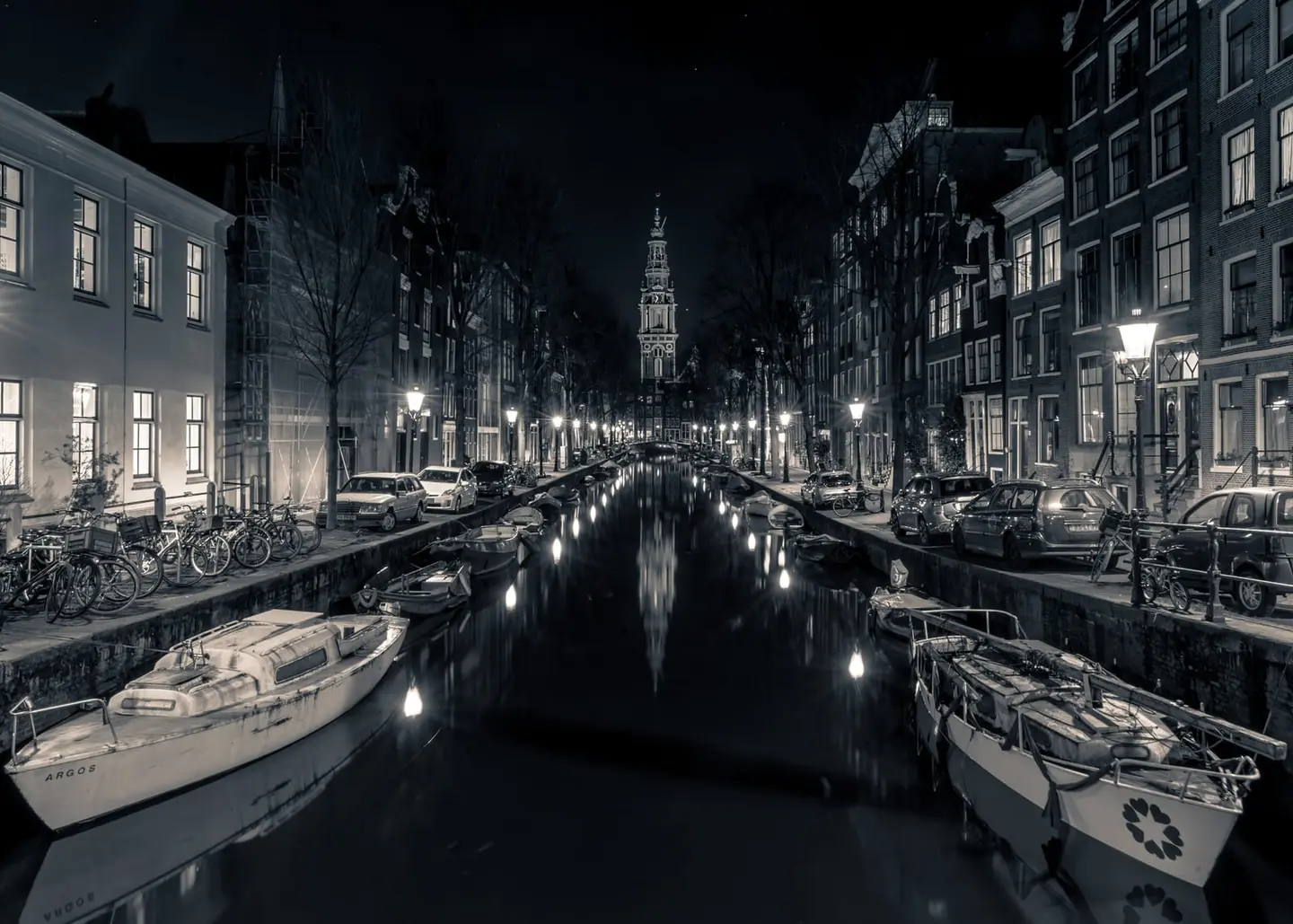 Looking down the symmetrical corridor of the Groenburgwal on a March night, the illuminated Zuiderkerk tower acts as a vanishing point for the entire composition — street lamps, canal boats, and…