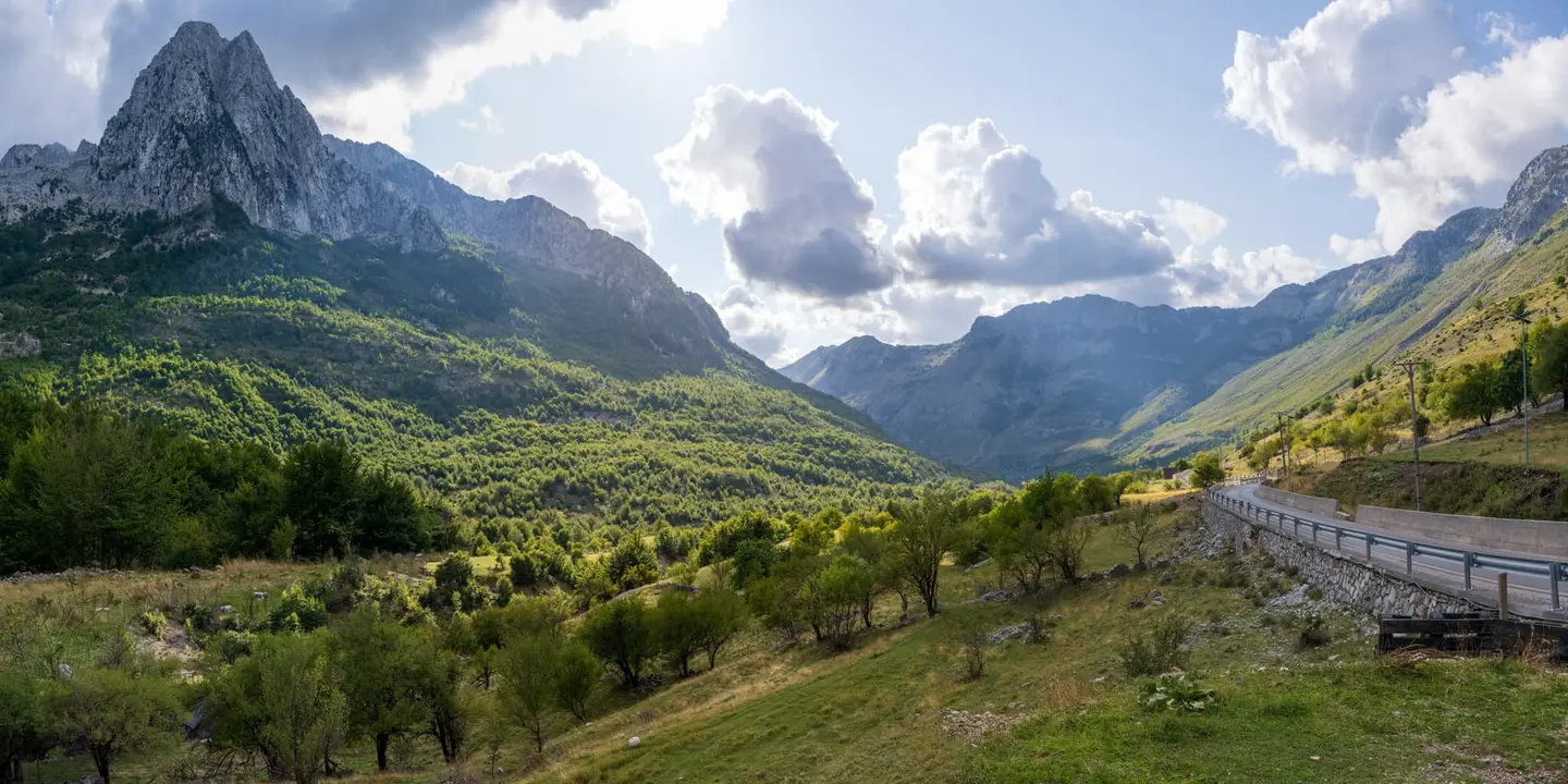A single dramatic limestone pinnacle dominates the left of the frame, rising directly out of a steeply-forested valley.