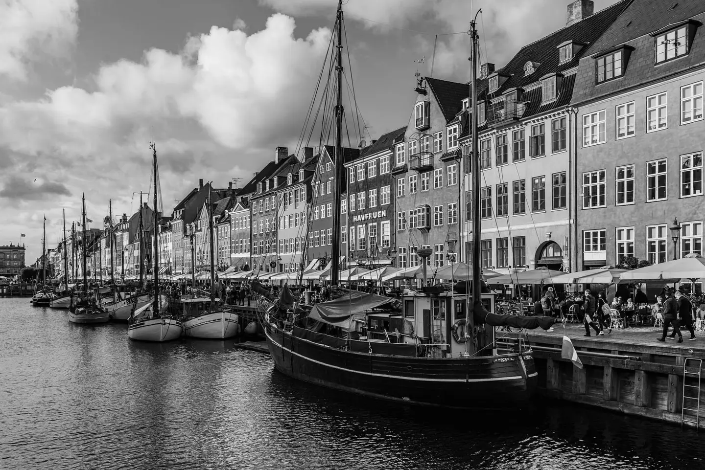 Historic wooden sailing ships rest along the quay of Nyhavn, Copenhagen's 17th-century canal harbour, their masts rising against a row of gabled townhouses.