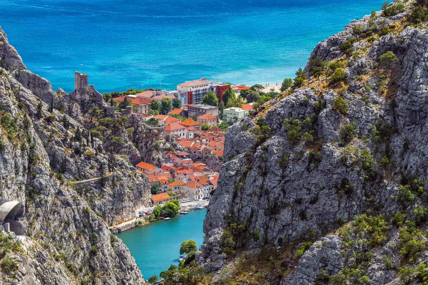 Turquoise water of the Cetina River winds through its final canyon stretch before emptying into the Adriatic, the renowned pirate fortress and historic town of Omiš spread across the gorge floor…