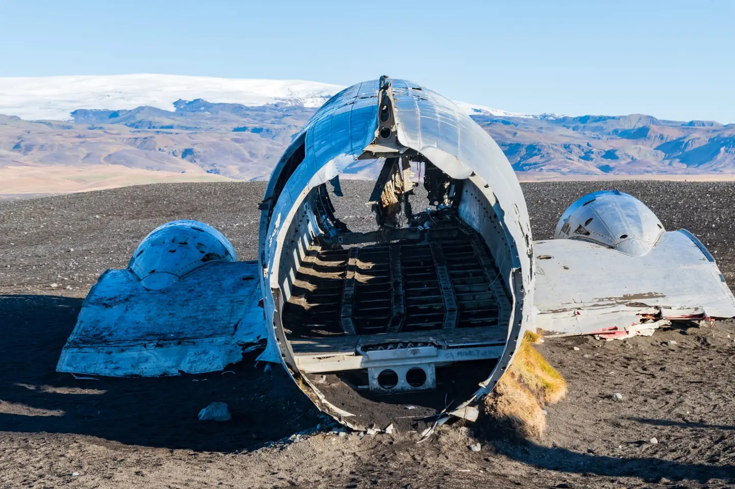 The stripped fuselage of the Sólheimasandur DC-3 rests on Iceland's black volcanic sands, its hollow ribs framing the dark desert and a snow-capped glacier beyond.