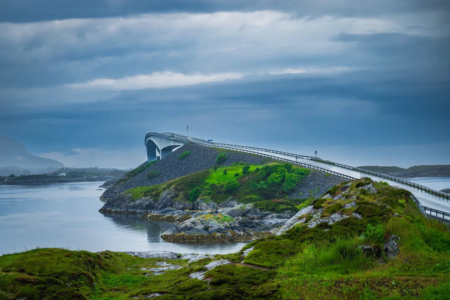 A dramatic modern bridge curves over lush islands and serene waters under a richly textured sky, capturing the essence of Norway’s Atlantic Road.