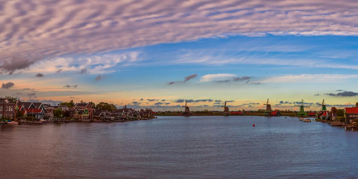 The wide Zaan river at Zaanse Schans reflects a soft pastel pink and blue evening sky scattered with mackerel clouds.